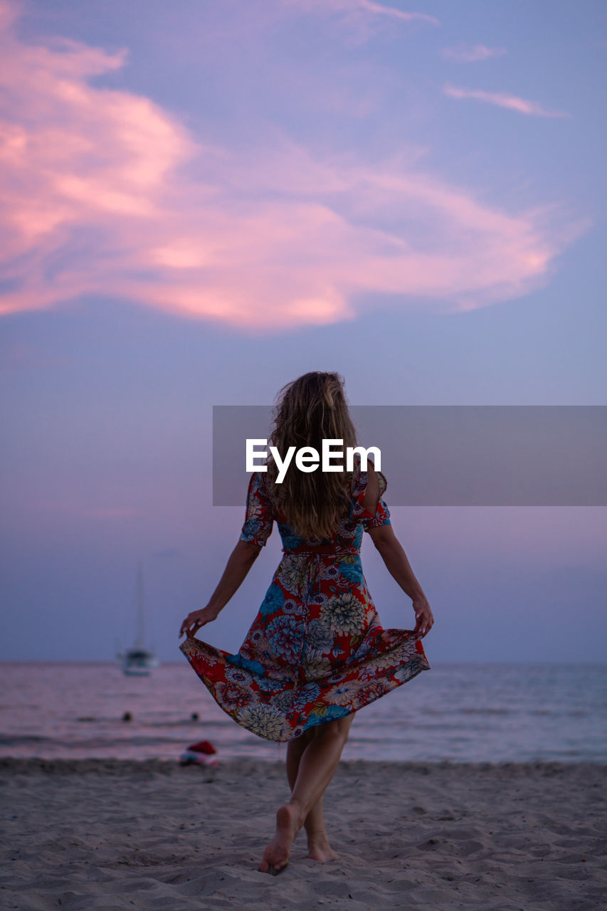 WOMAN ON BEACH AGAINST SKY DURING SUNSET