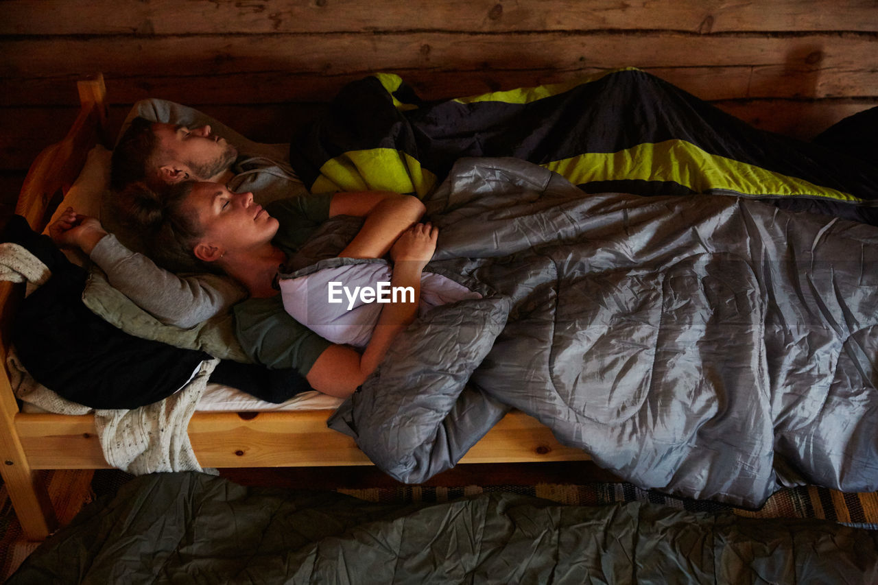 High angle view of couple with blankets sleeping on bed in log cabin