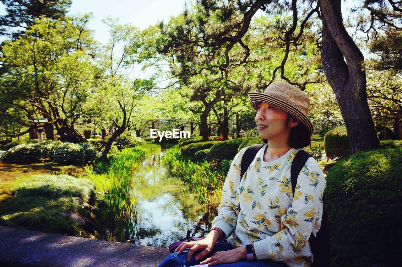 Smiling woman looking away while sitting against plants at park