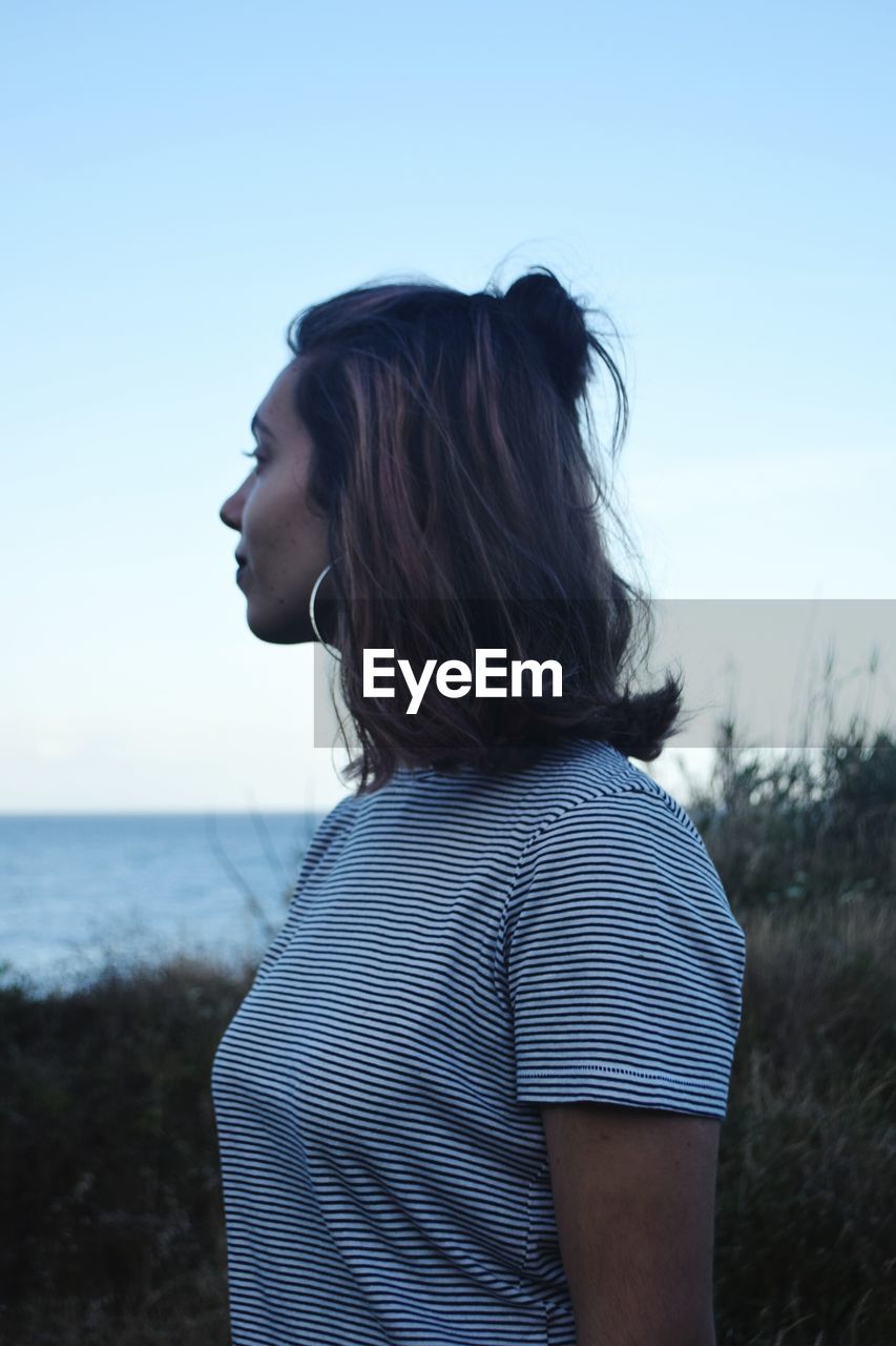 Side view of young woman standing on field against sky at dusk