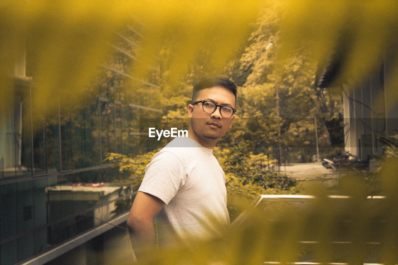 Thoughtful man wearing eyeglasses seen through leaves