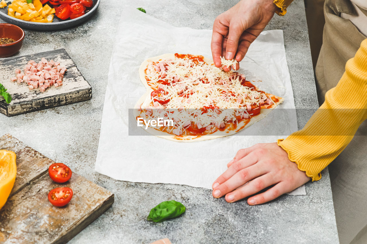 Hand of caucasian teenage girl pouring grated cheese on pizza hearts for valentine's day.