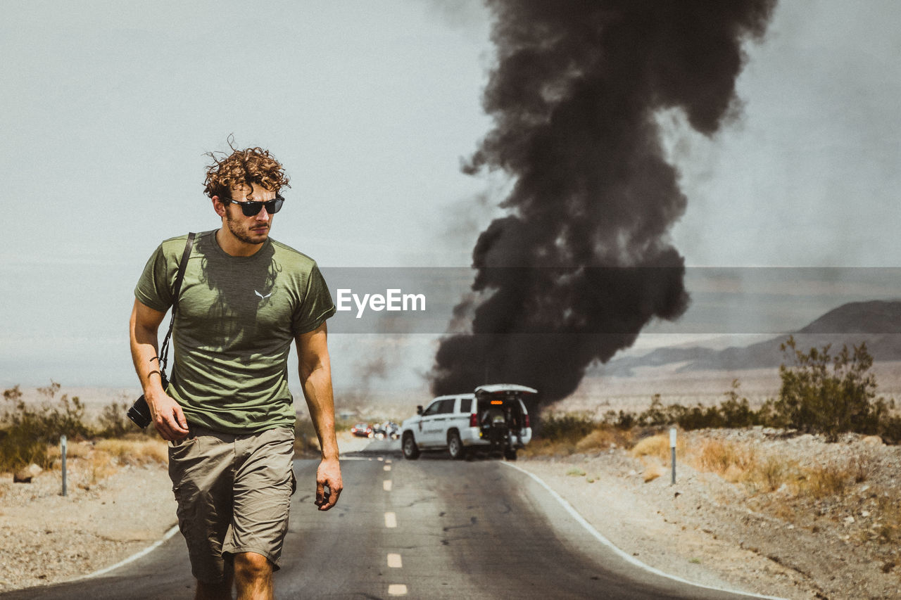 Young man walking on road against burning car