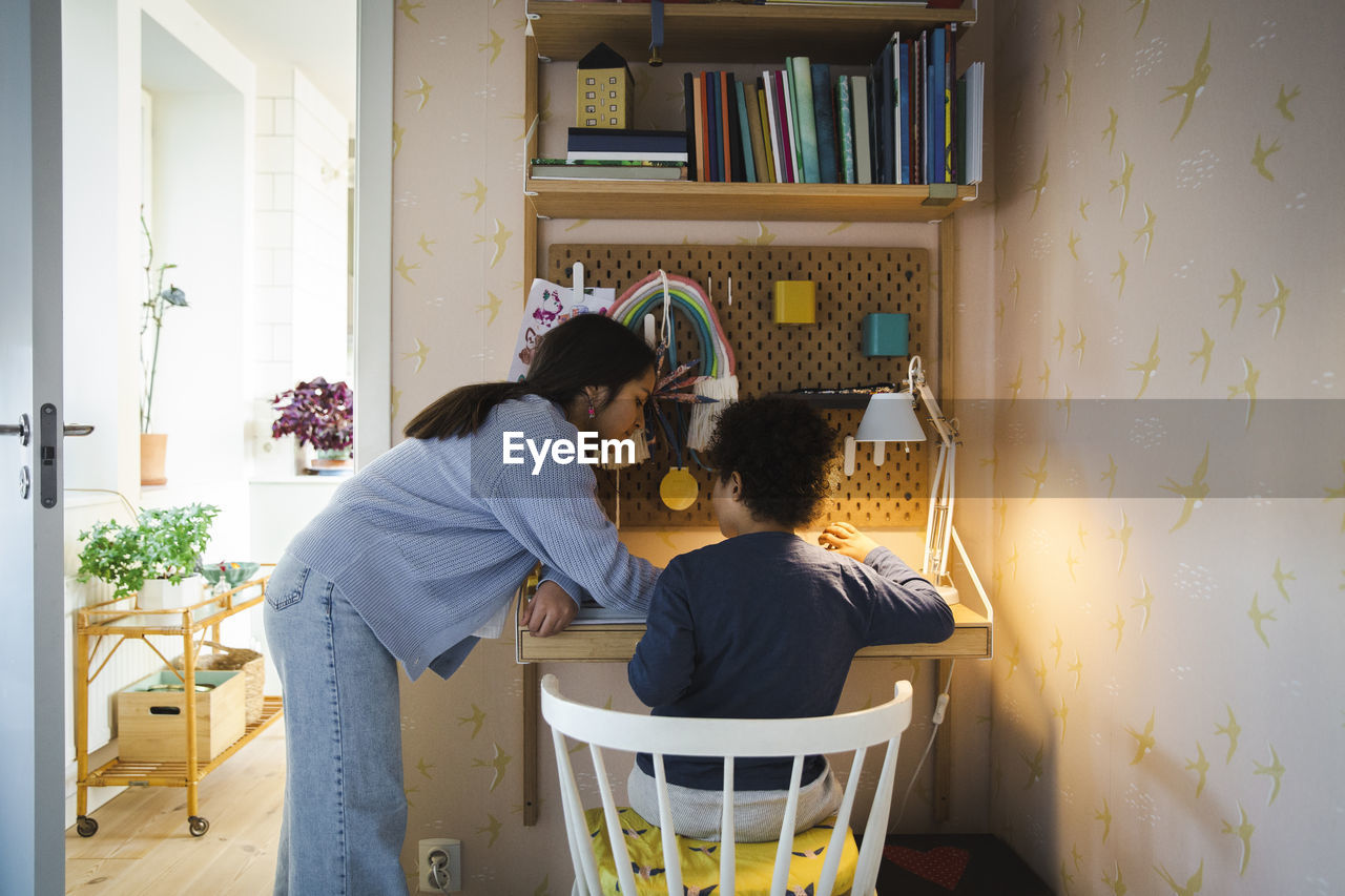 Side view of sister helping brother while studying at home