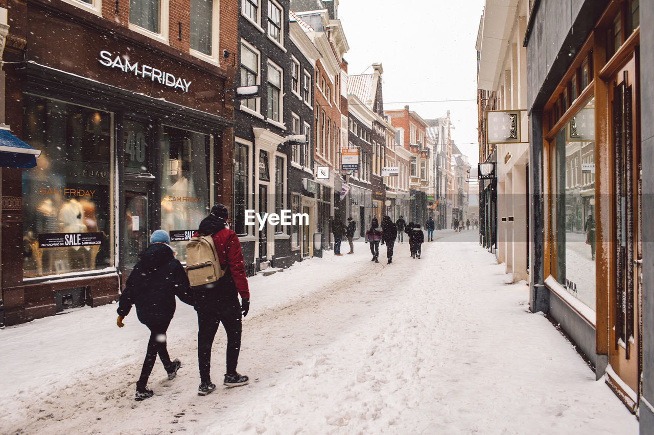 PEOPLE WALKING ON STREET AMIDST BUILDINGS DURING WINTER