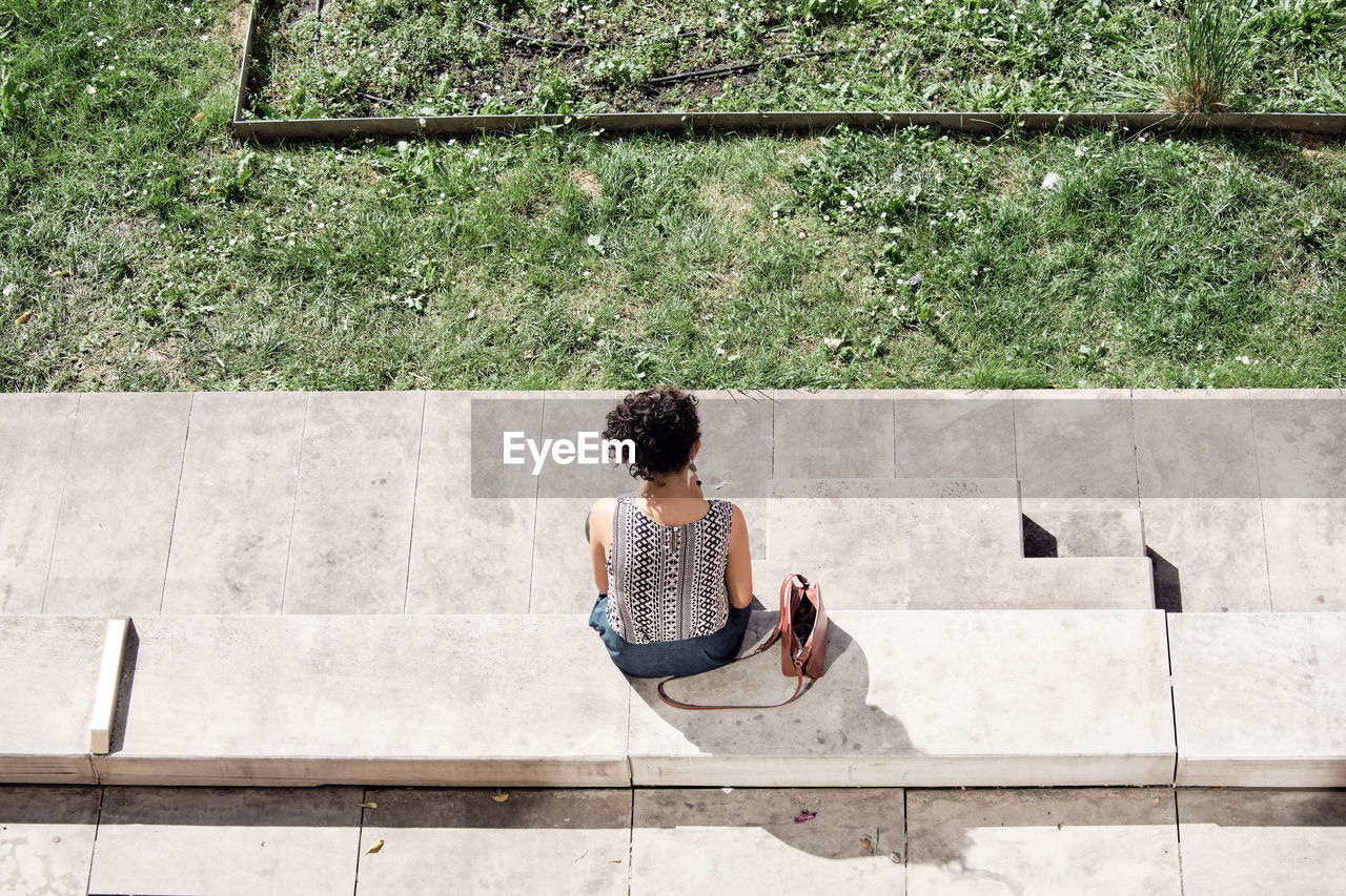 FULL LENGTH REAR VIEW OF WOMAN SITTING ON WALL