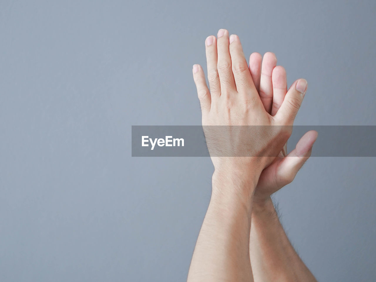 Cropped hand of man clapping against gray background