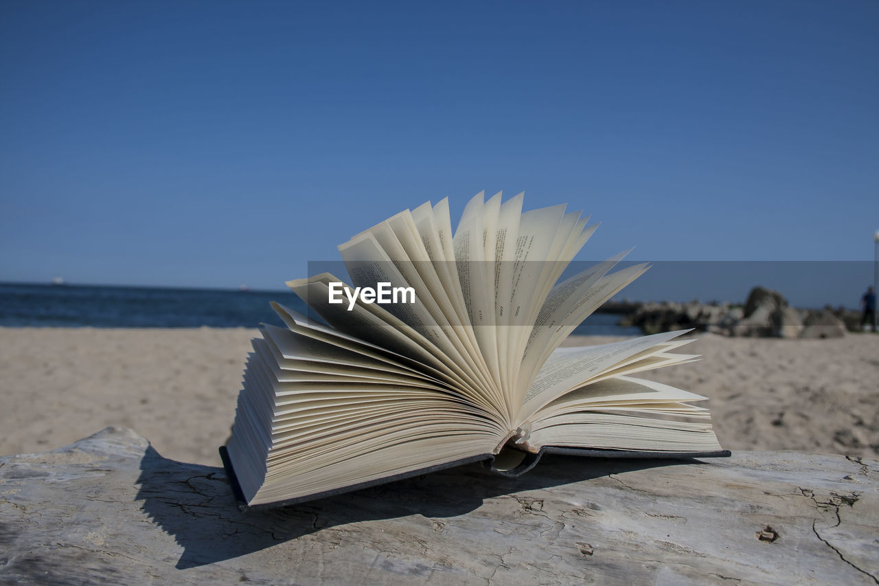 Close-up of book on beach against clear sky