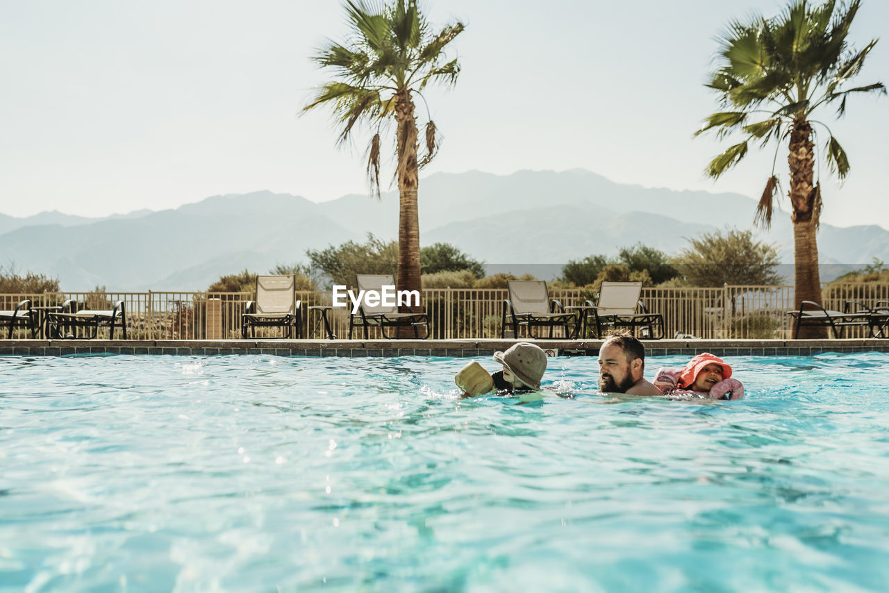 Dad and young children swimming in large california pool on vacation