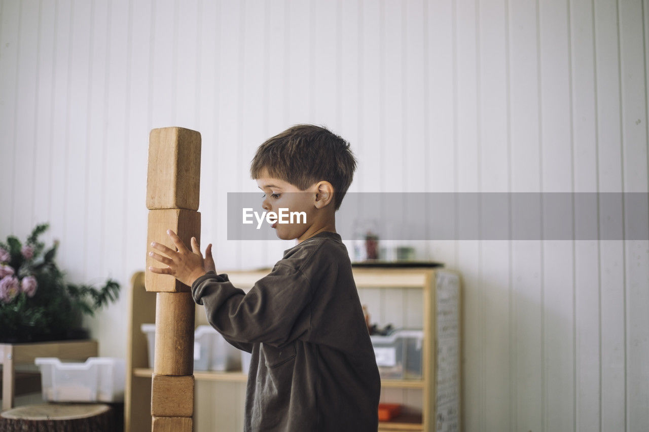 Side view of boy stacking toy blocks while playing in classroom at kindergarten