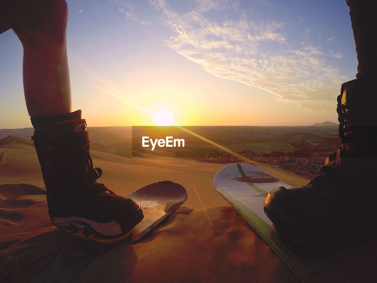 Low section on men on sandboard at desert during sunset