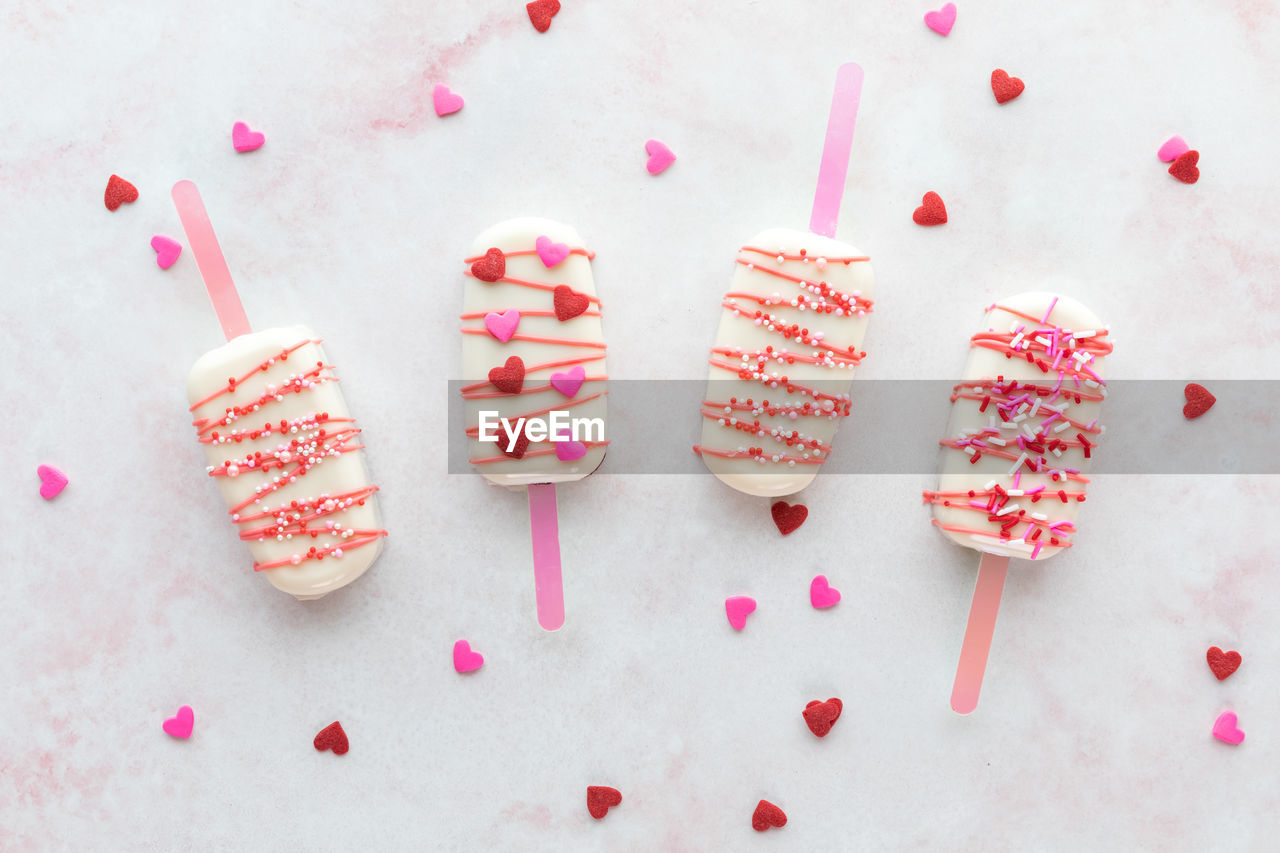 Valentine's day cakesicles with sprinkles on a pink marble surface.