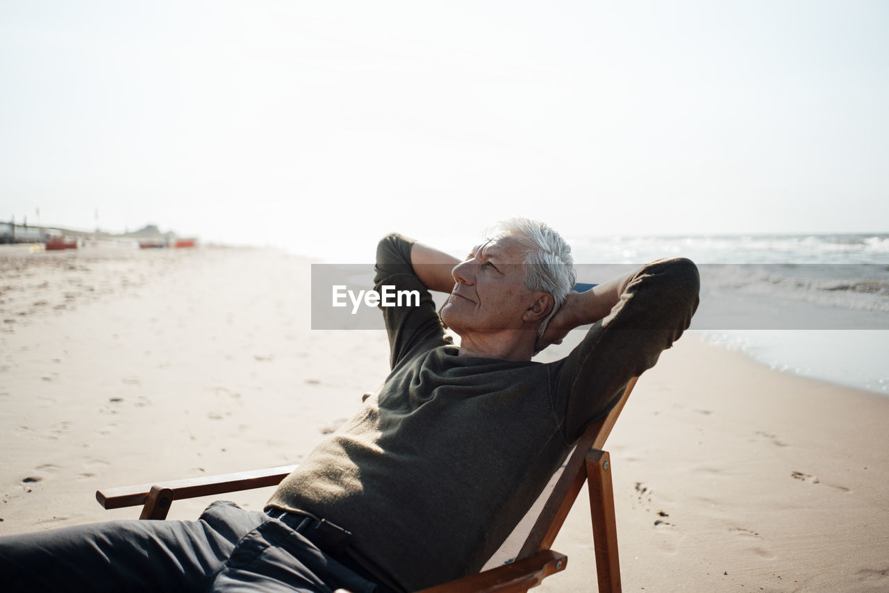 Senior man with hands behind head relaxing on chair at beach