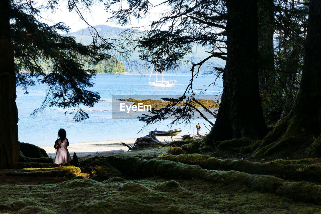 MAN SITTING ON TREE BY LAKE