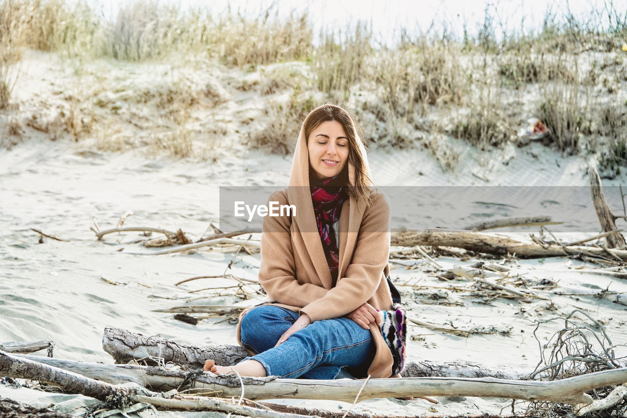 Girl wrapped in a warm coat sitting on the cold autumn beach person