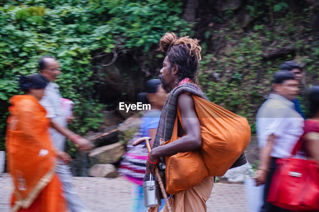 Side view of sadhu with bag walking by people on street