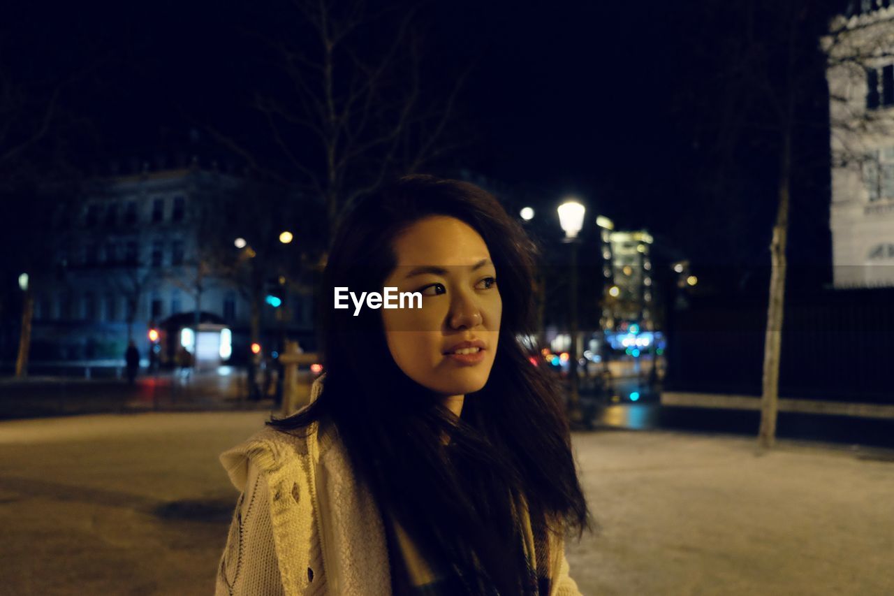 Portrait of young woman standing in city at night