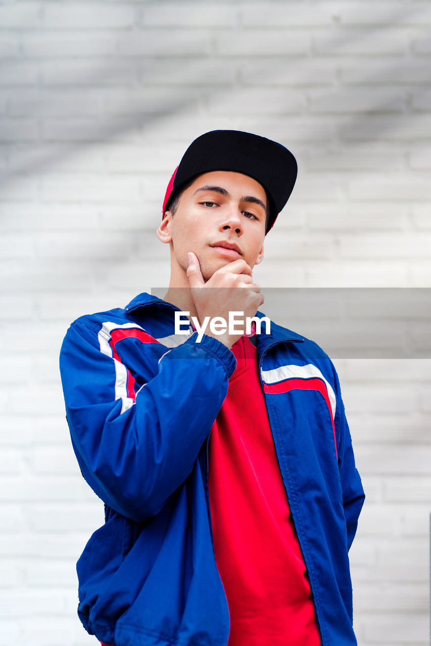 A teenage boy agains white brick wall. a male teenager model wearing casual clothing. 