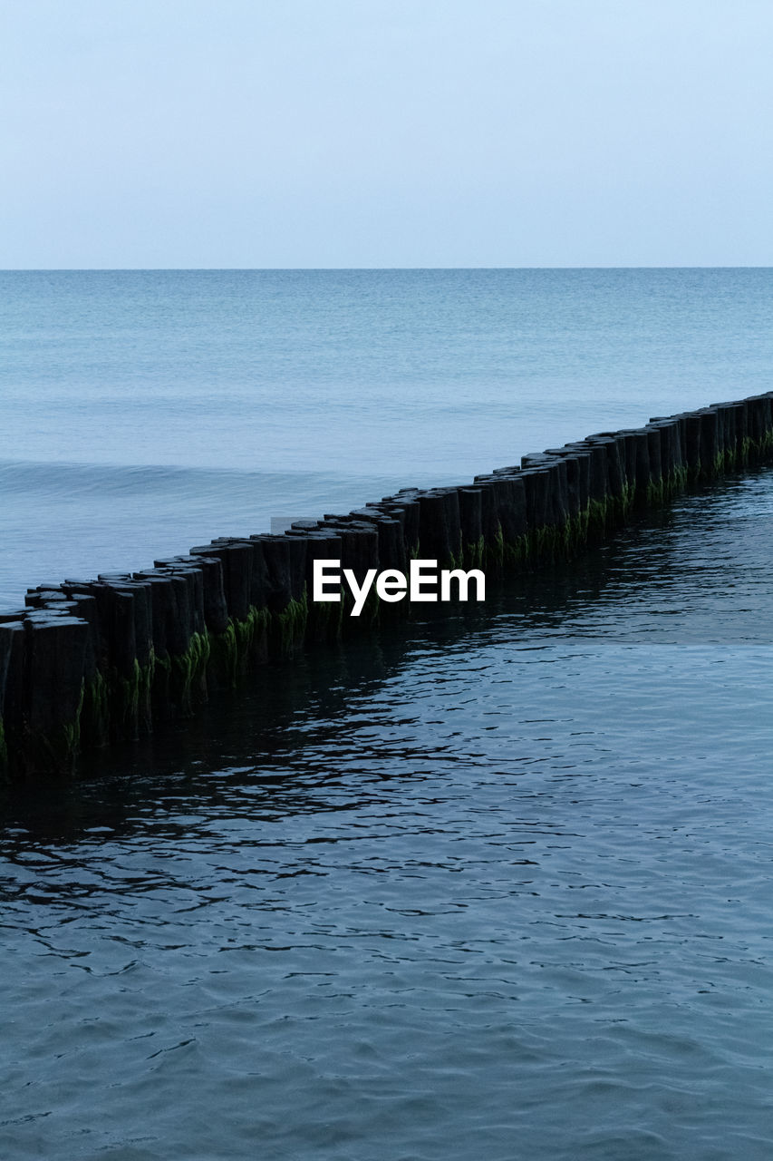 Scenic view of sea with diagonal groyne against clear sky