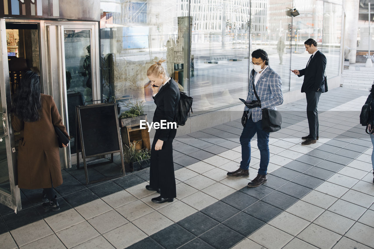 People standing in line outside cafe keeping distance