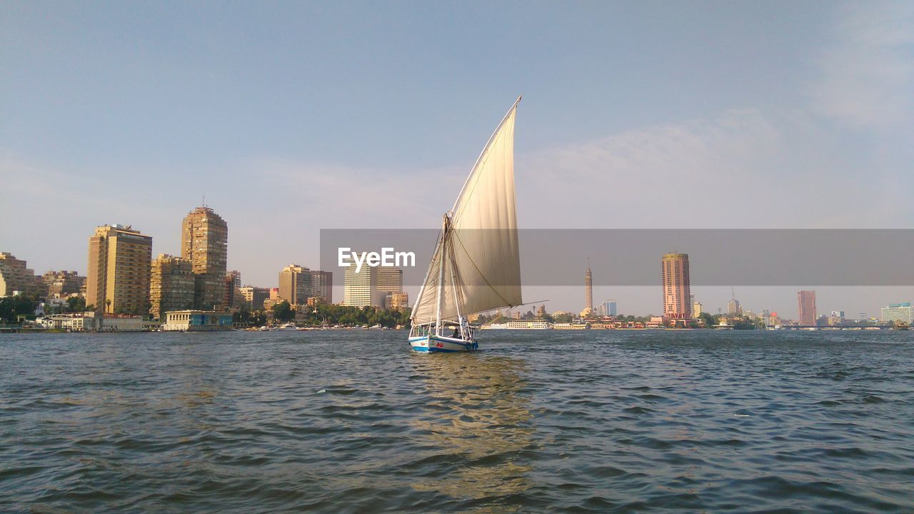 Sailboats in sea by modern buildings against sky