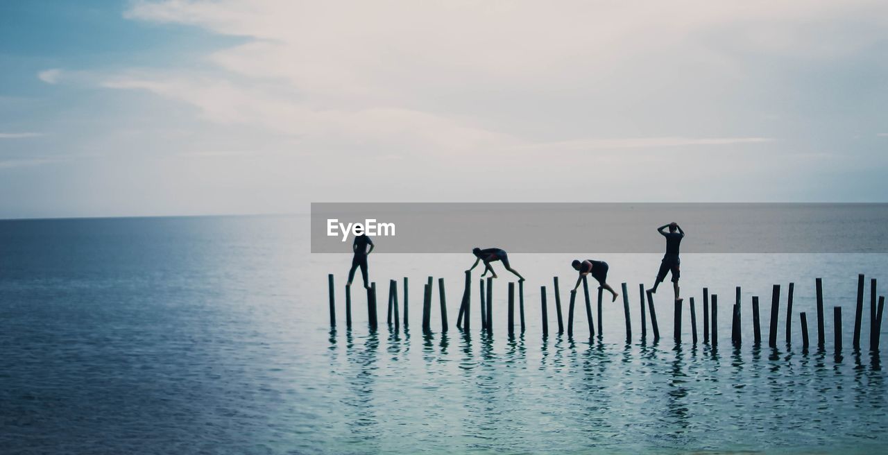 Friends walking on wooden posts in sea