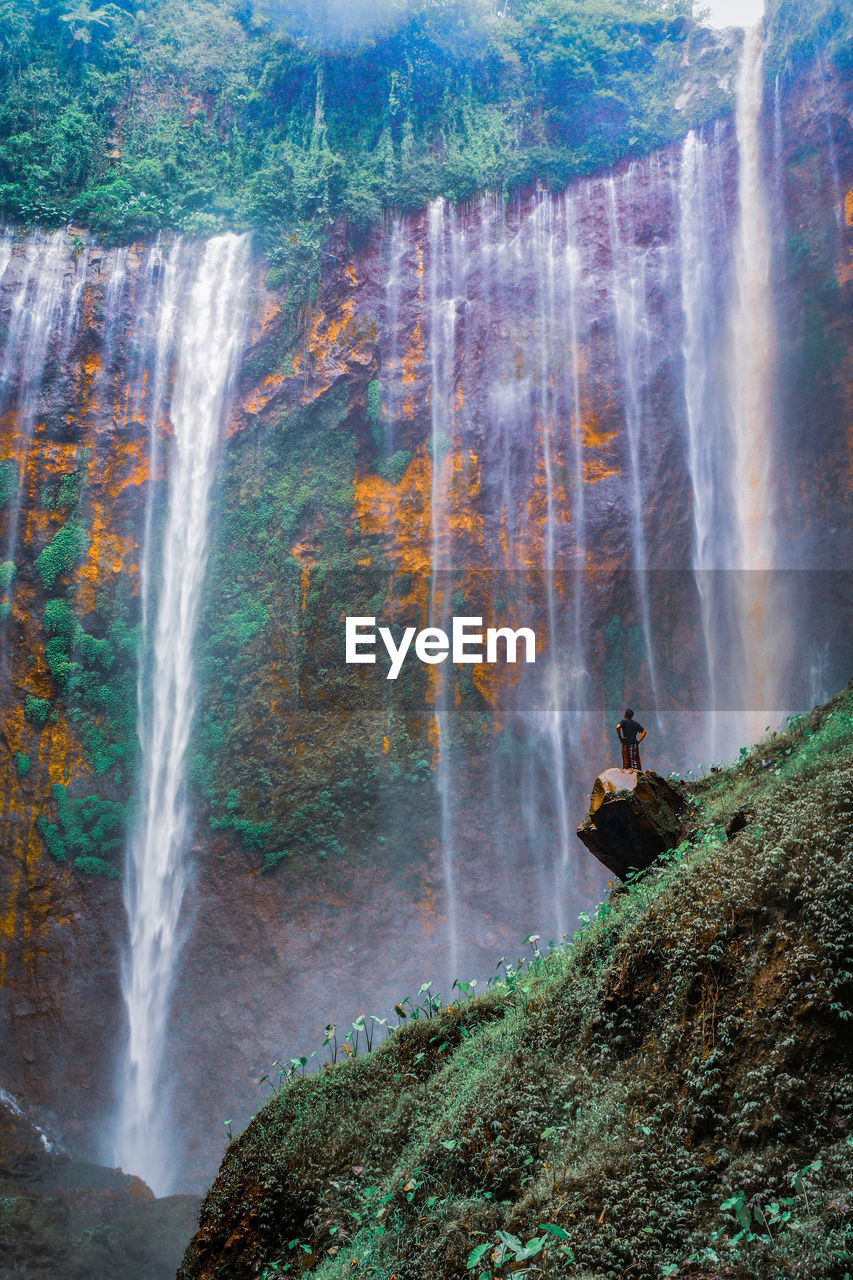 Scenic view of waterfall with man standing on rock