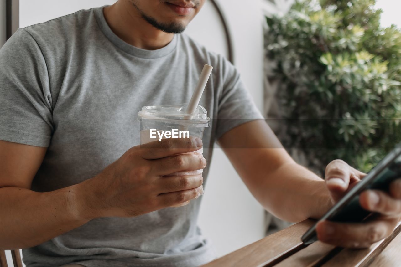 midsection of man using mobile phone while sitting on table