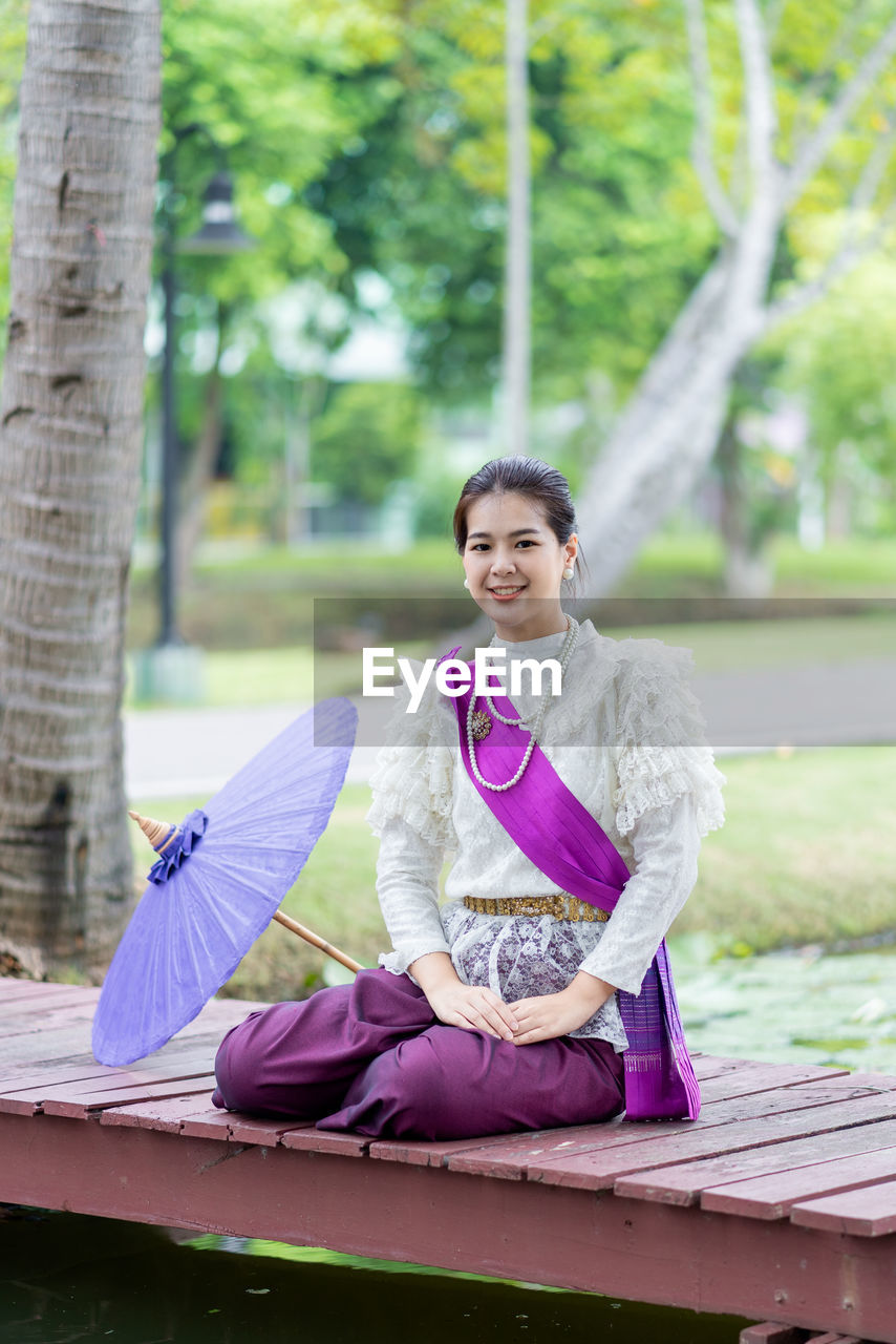 Portrait of smiling young woman sitting on footbridge