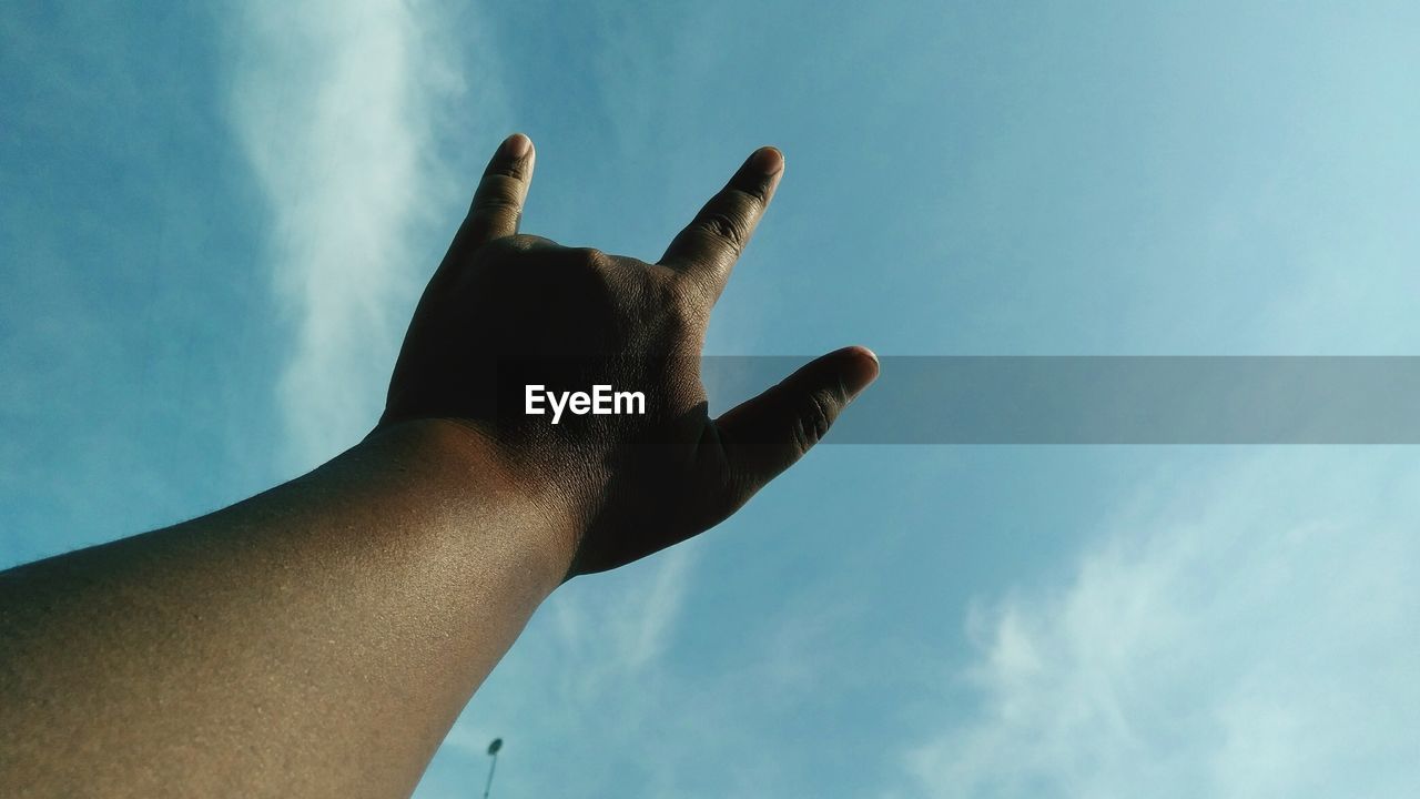 Low angle view of hand gesturing against sky