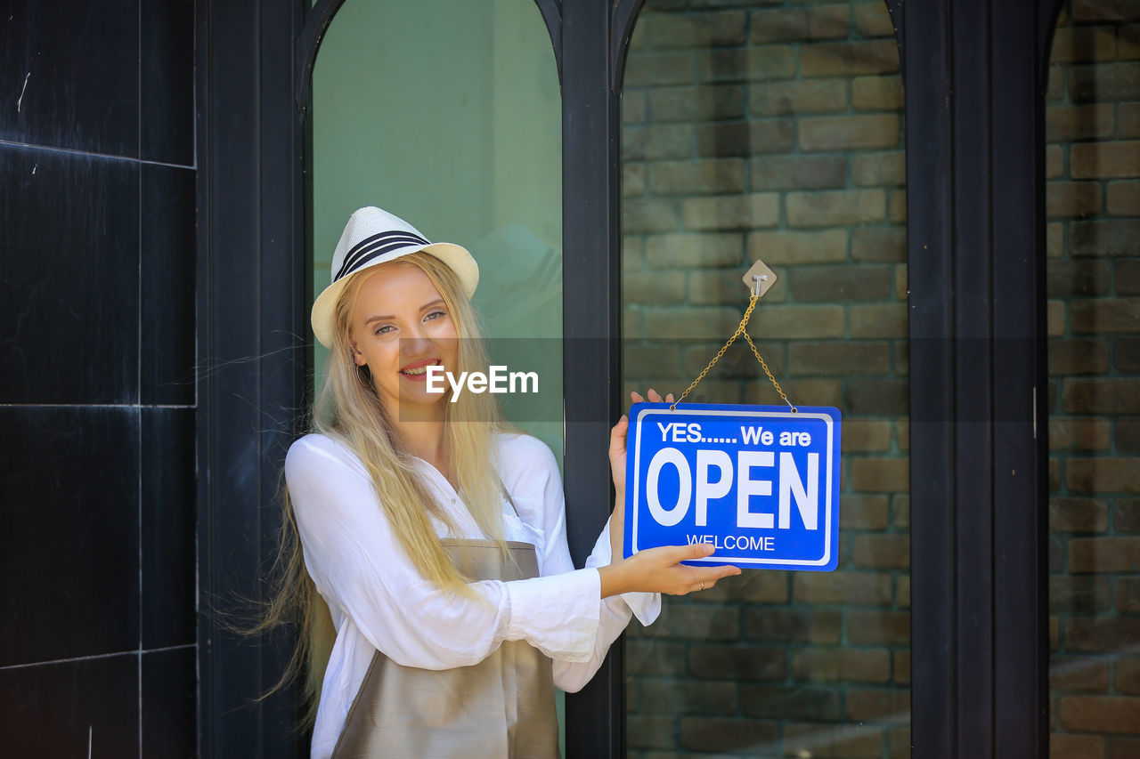 Beautiful blonde hair girl standing with confidence in front of open shop.