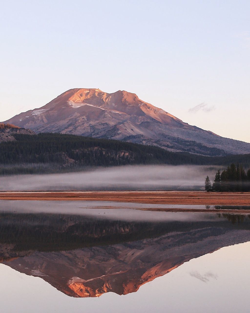 Reflection of rocky mountain against clear sky at morning