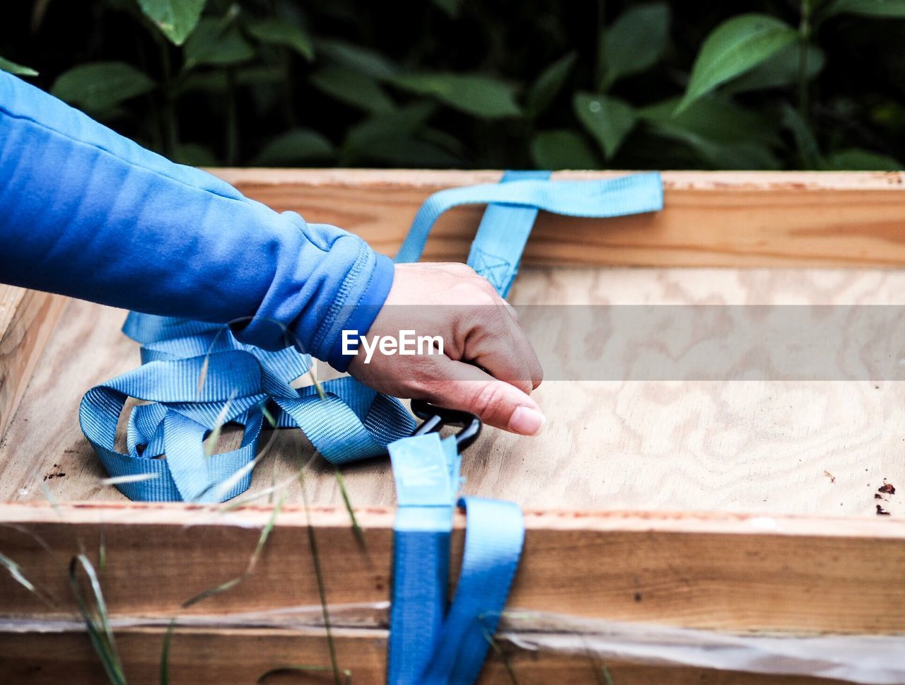 Cropped hand holding blue strap on wooden box