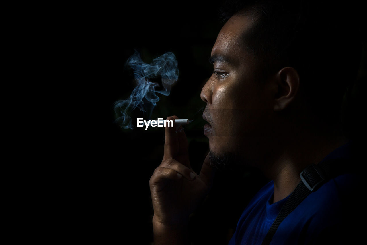 Close-up of man smoking cigarette against black background