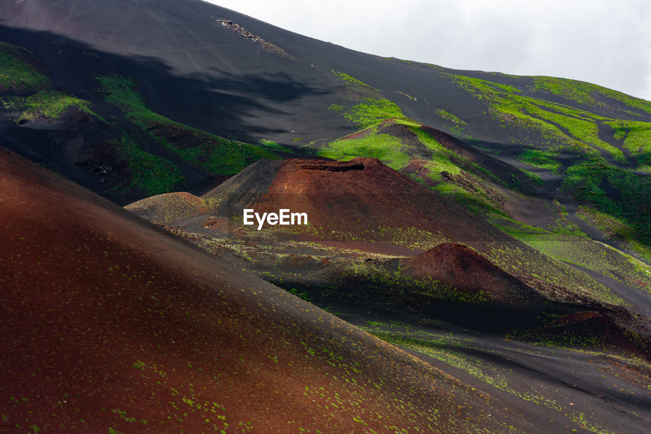 Breathtaking scenery of etna mountain. red volcanic sand and green vegetation with clouds shadows. 