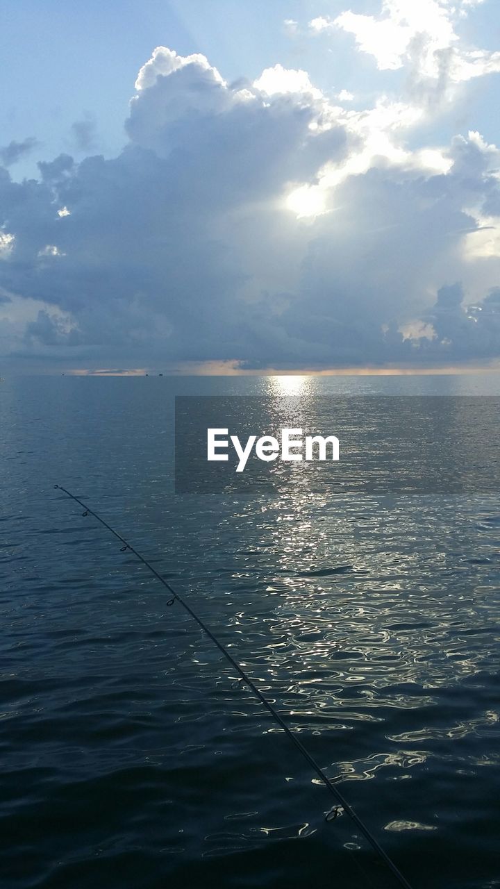 Fishing rod over sea against cloudy sky