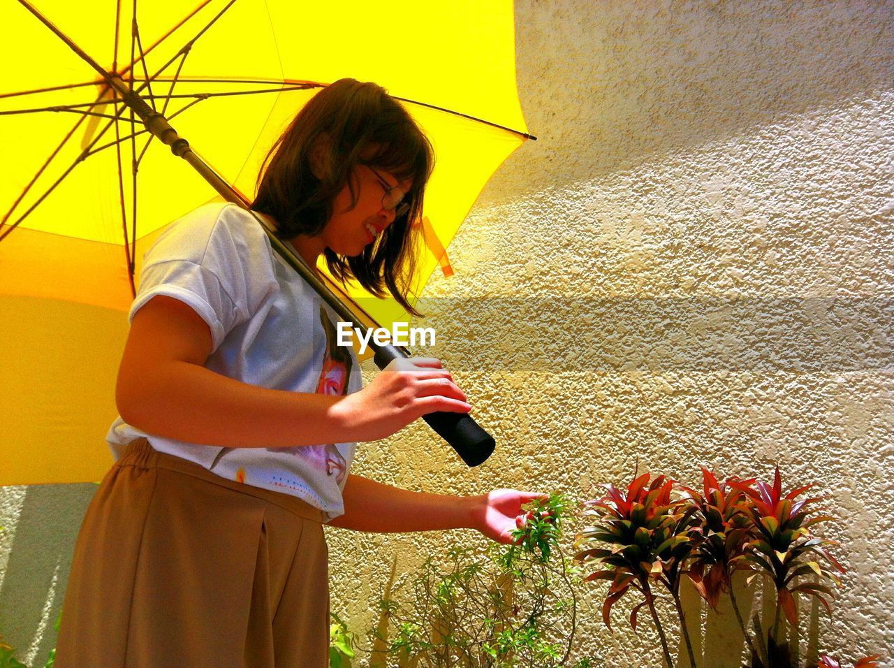 WOMAN HOLDING UMBRELLA WHILE STANDING BY YELLOW WALL