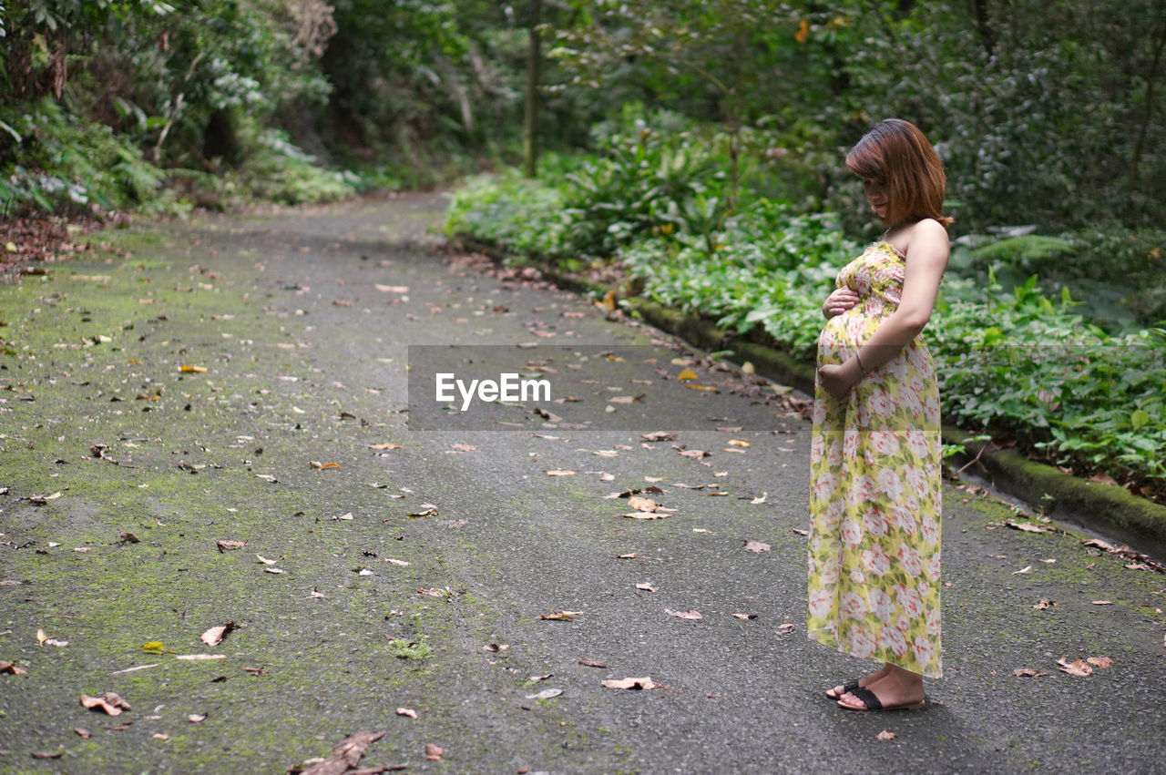 Full length of pregnant woman standing on road in forest