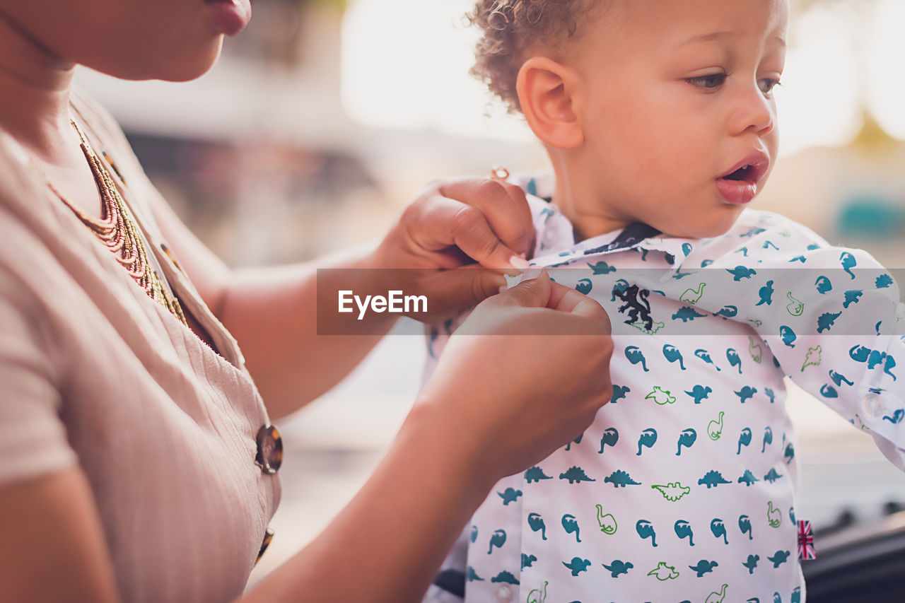 Mom buttoning baby boy's shirt, close up to hands and boy's face.