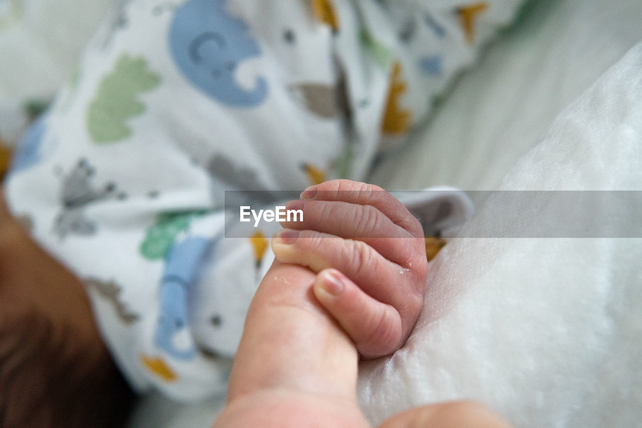 CROPPED IMAGE OF HAND HOLDING BABY ON BED WITH TATTOO