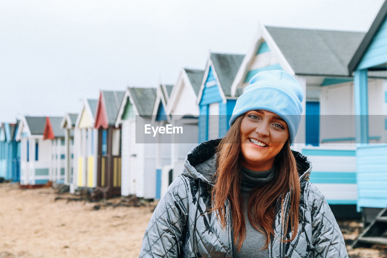 Portrait of smiling young woman standing against beach huts