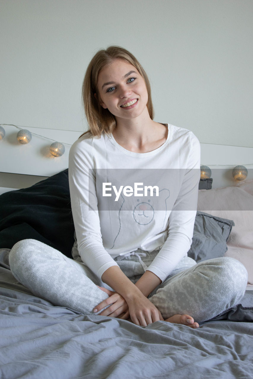 PORTRAIT OF A SMILING YOUNG WOMAN SITTING ON BED AT HOME