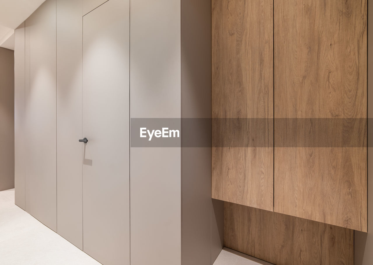 Apartment corridor with wooden wardrobe and grey panel walls with door.