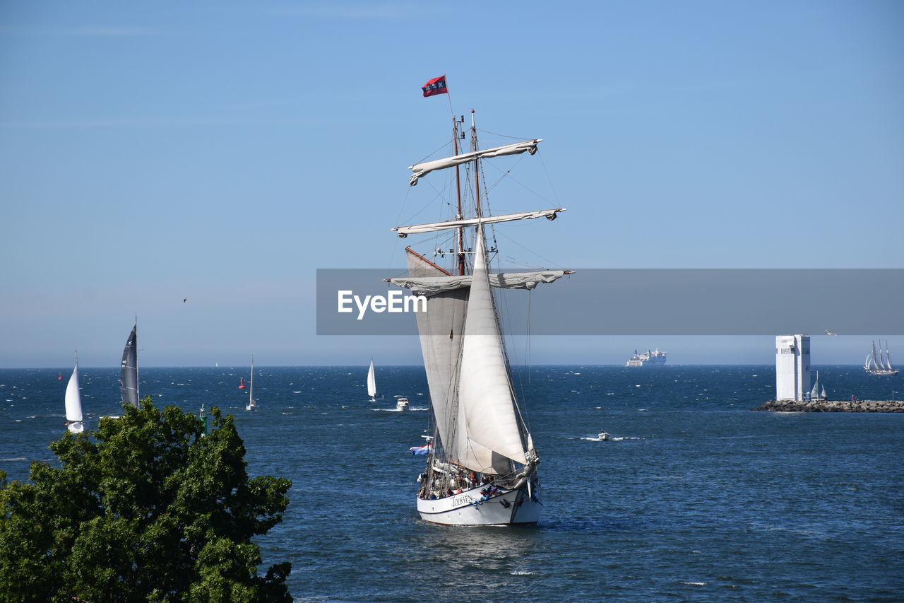 water, sea, nautical vessel, transportation, sky, nature, vehicle, sailboat, sailing ship, ship, sailing, mode of transportation, wind, day, ocean, boat, no people, blue, mast, architecture, flag, watercraft, travel, pole, clear sky, outdoors, horizon over water, coast, environment, horizon, tall ship, tower, beauty in nature, travel destinations, sunny, scenics - nature