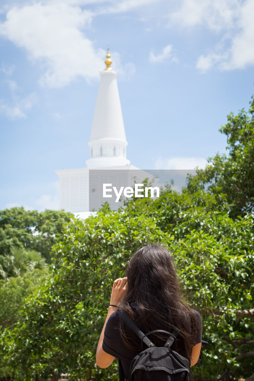 Rear view of woman with taking photo of temple against sky