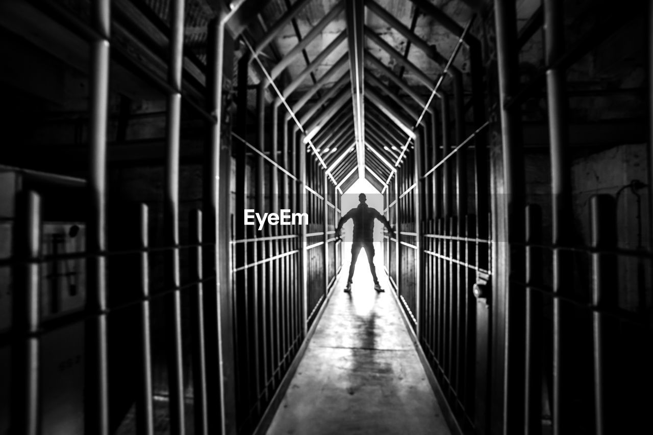 FULL LENGTH REAR VIEW OF MAN WALKING ON FOOTBRIDGE