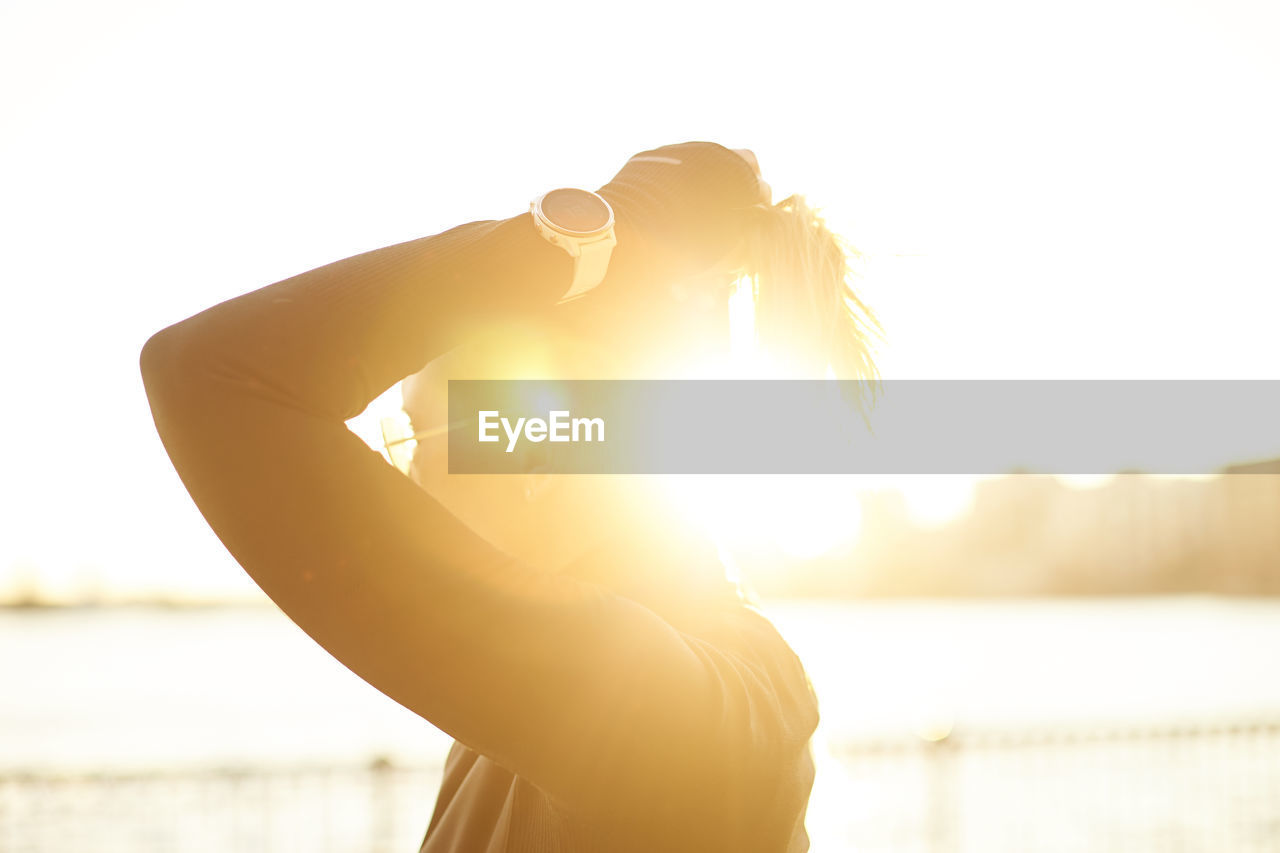 An athletic woman putting her hair up backlit by the sun.