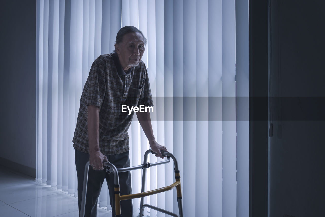 Disabled man walking by blinds with walker 