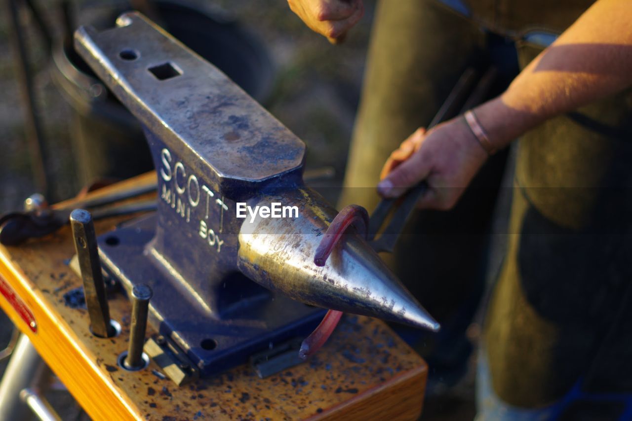 Midsection of blacksmith holding horseshoe on anvil