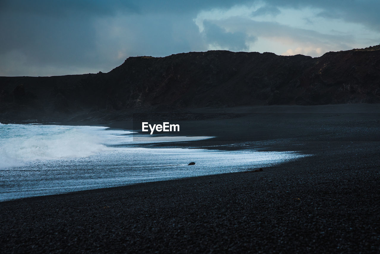 Scenic view of black sand beach against mountains and sky during sunset